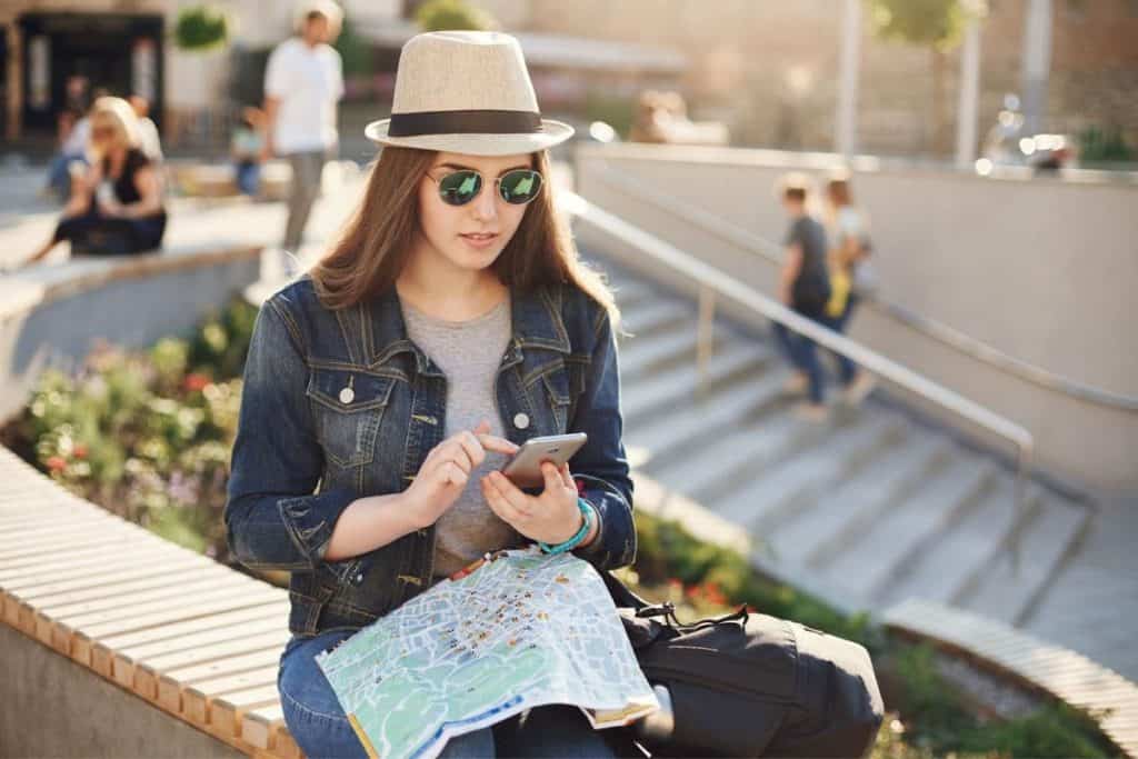 Young traveler using cell phone and map to plan her journey online