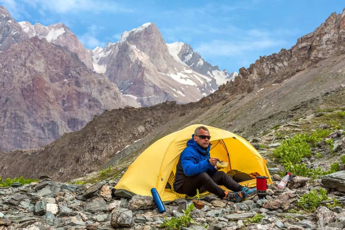 a backpacker eating on a mountain with a set up tent.