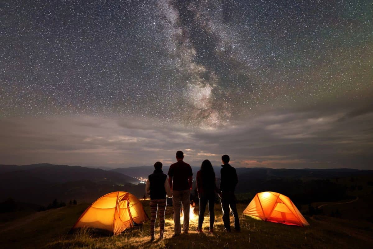 a group of four people in sillhoutte looking at the night sky milky way camping
