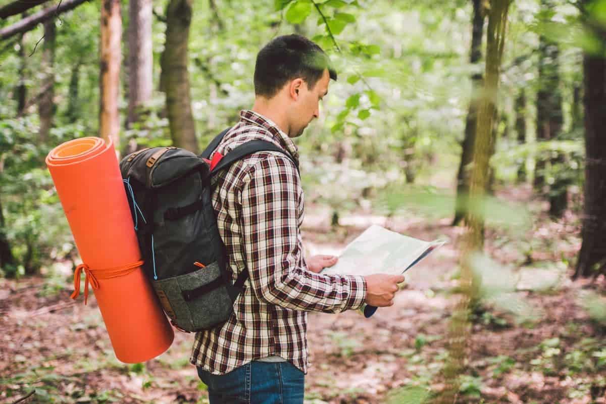 Man with Backpack and map searching directions in wilderness area. Tourist with backpack using map in forest. concept tourism holidays. Hiking man.