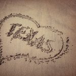 Texas and heart written on beach sand.