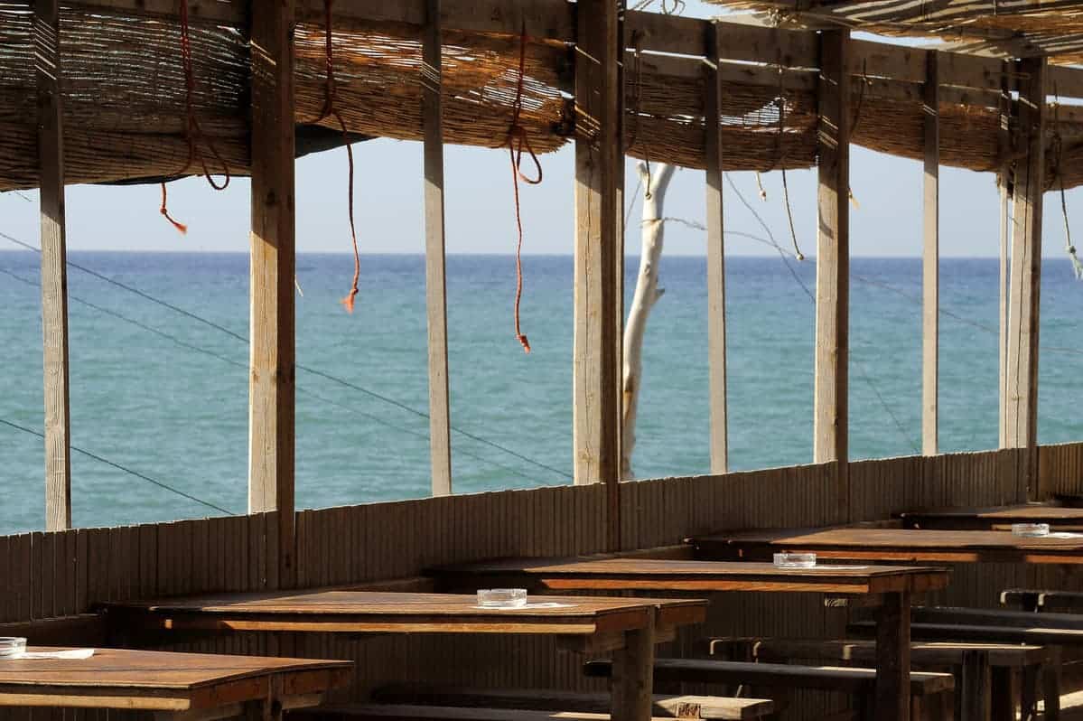 a wooden tables and chairs outside with a view of the ocean.